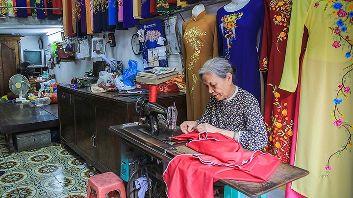 A Vietnamese tailor adjusting an Ao Dai in a traditional workshop