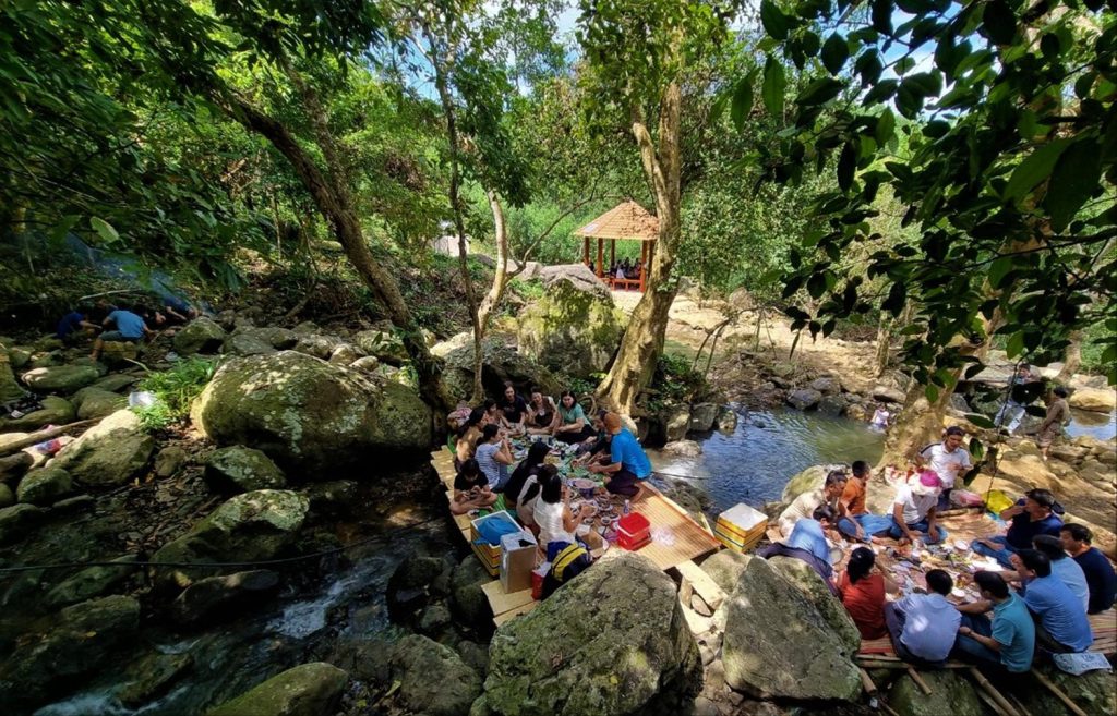 Group enjoying lunch on a picnic mat near the stream